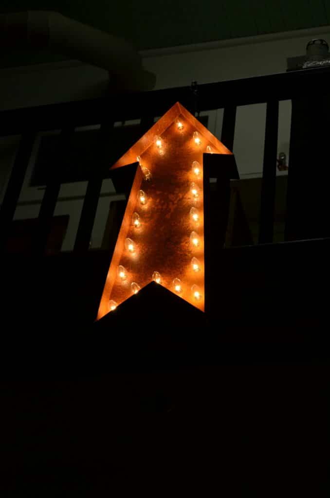 Glowing neon arrow sign pointing upwards in dimly lit interior setting.