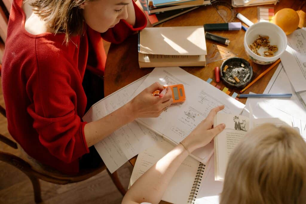 Two students engaged in studying at a table with textbooks, notes, and stationery.
