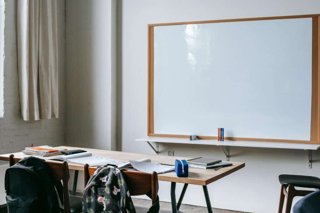 An empty classroom with wooden desks, chairs, and a large whiteboard for teaching.