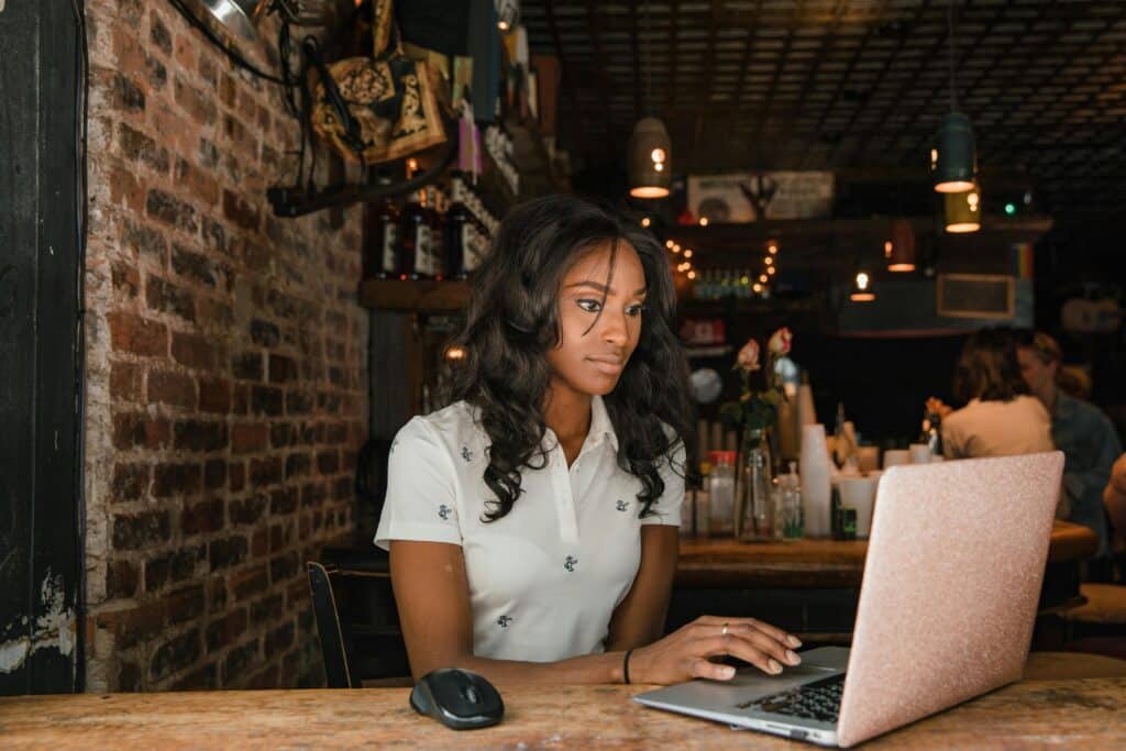 A woman focused on her laptop inside a cozy café setting, surrounded by a warm and atmospheric interior.