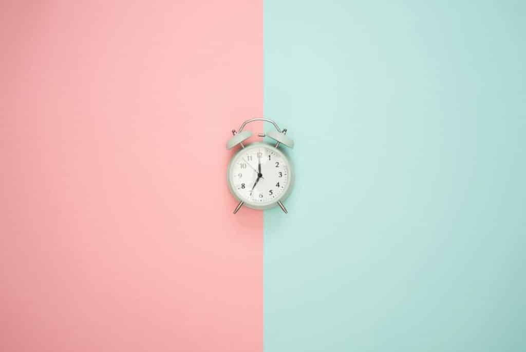 A vintage round clock on a split pastel pink and blue background.