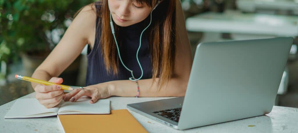 A young woman takes notes while studying with a laptop. Ideal for educational and lifestyle concepts.
