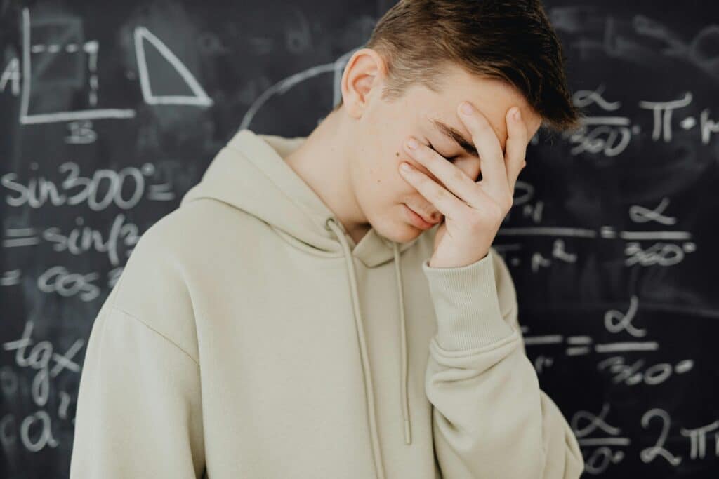 Young man overwhelmed by mathematical calculations on a blackboard in a classroom setting.