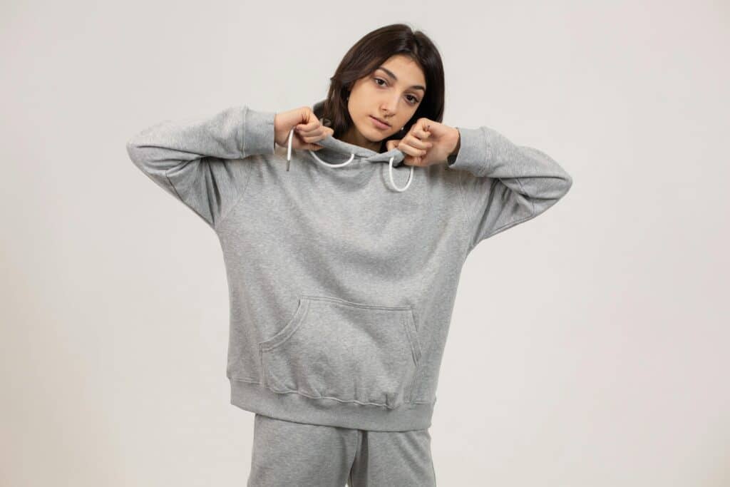 Serious female wearing oversize hoodie and sweatpants standing against white background and looking at camera