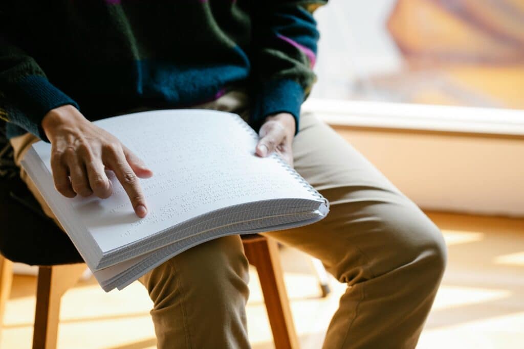 Close-up of a person reading a Braille book in natural light indoors, highlighting sensory interaction.