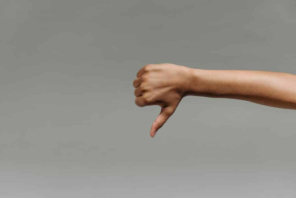 Close-up of a person's hand giving a thumbs down gesture against a gray background.