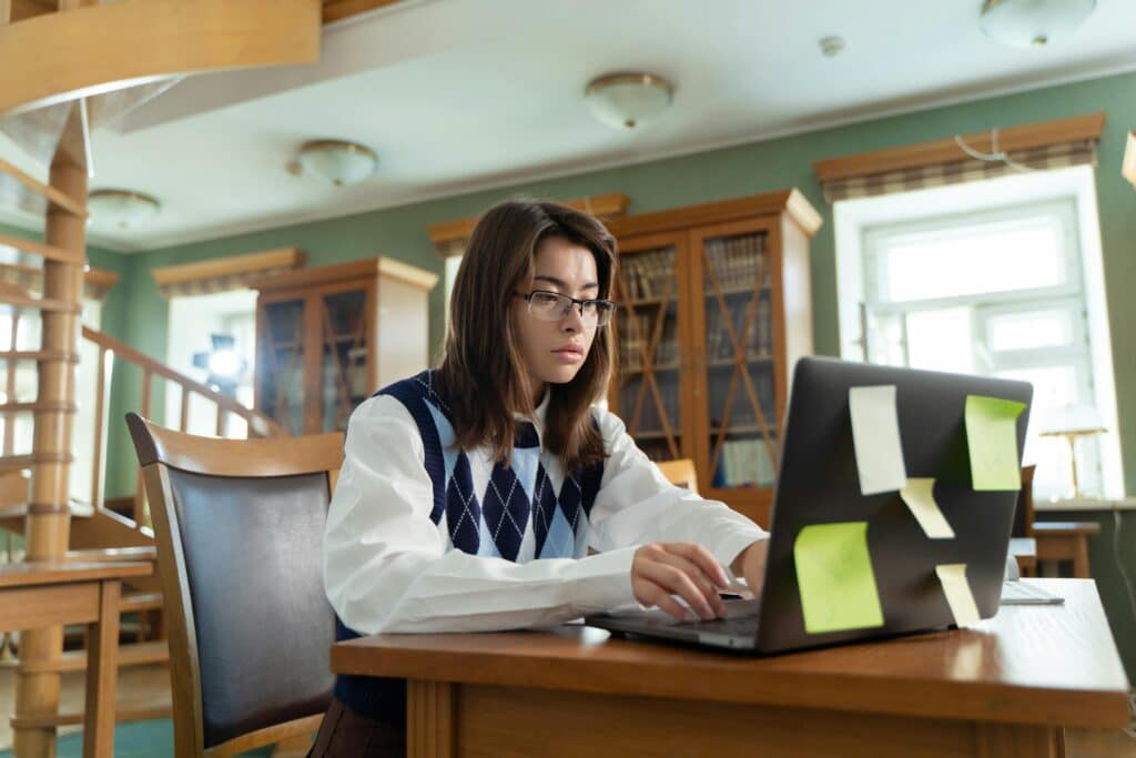 Young woman intensely studying on laptop in a university library setting.
