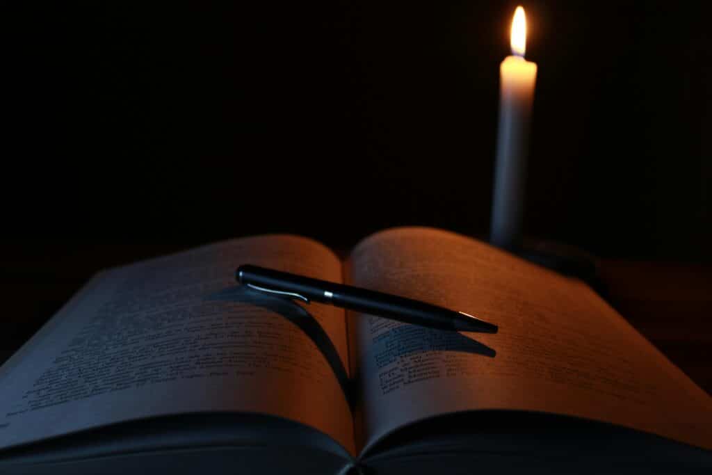 An open book and pen on a desk illuminated by candlelight, creating a tranquil study atmosphere.