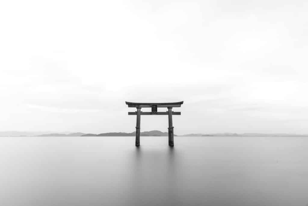 Serene black and white image of a torii gate standing in calm waters, symbolizing tranquility.