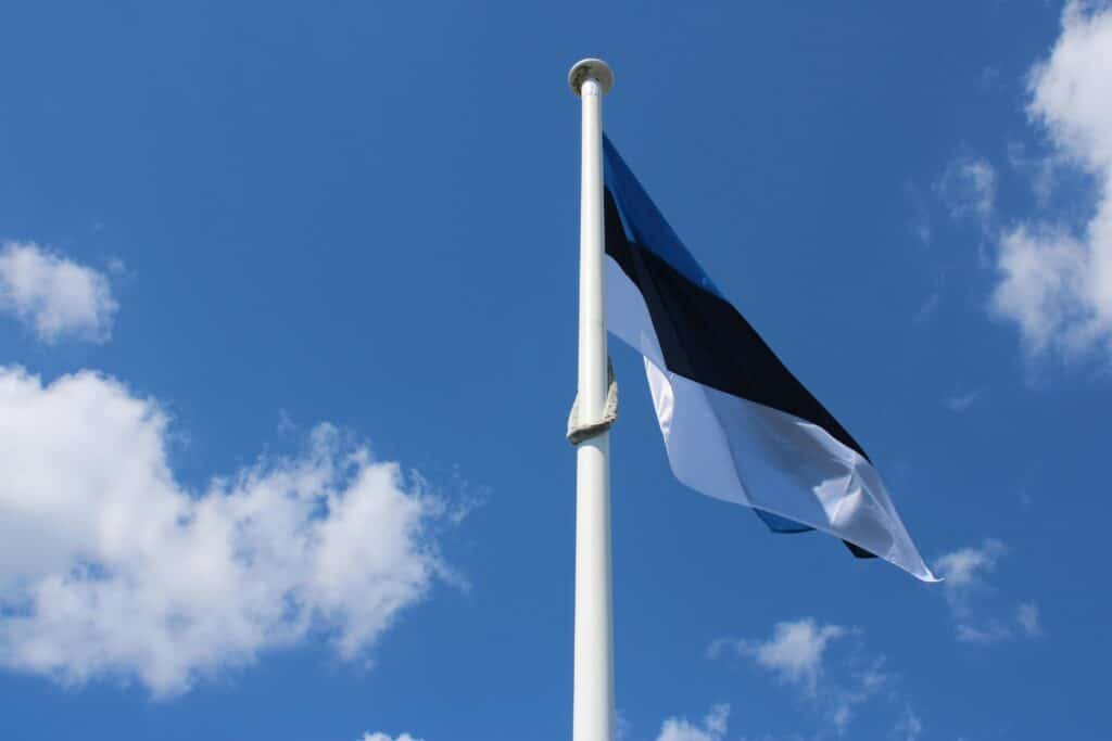 High view of Estonian flag fluttering against a vibrant blue sky with scattered clouds.