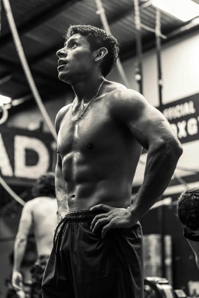 Black and white photo of a fit man resting in a gym, showcasing muscles and determination.