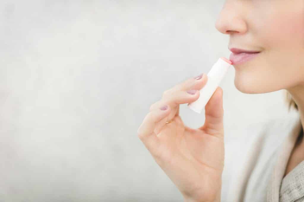 Close-up of a young woman applying lip balm for lip care and protection.