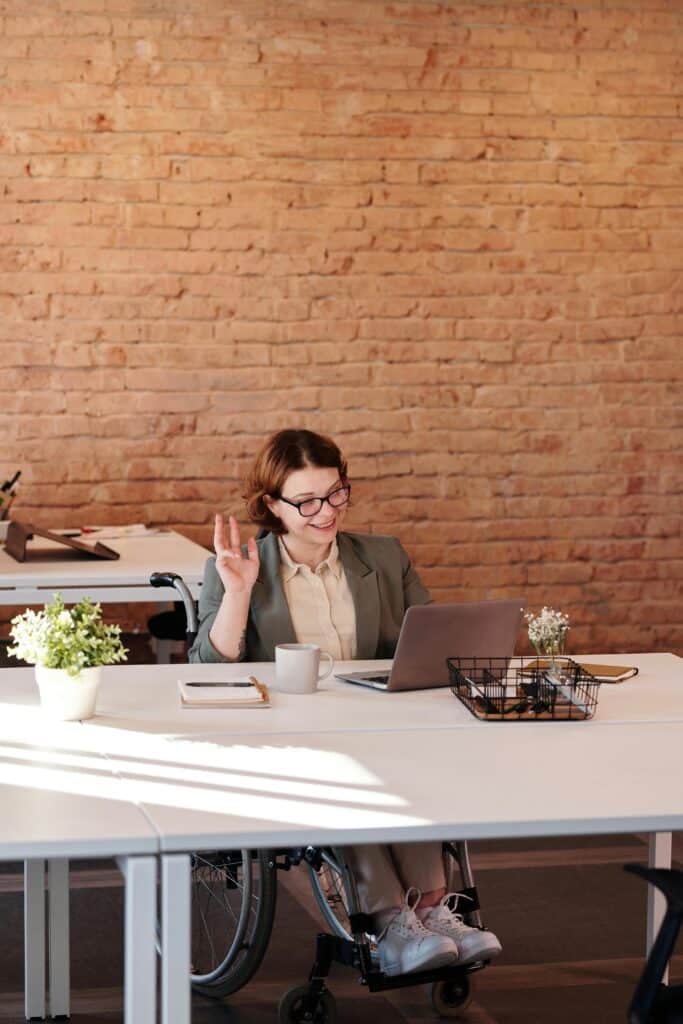 A cheerful businesswoman in a wheelchair working remotely from a modern office setting.