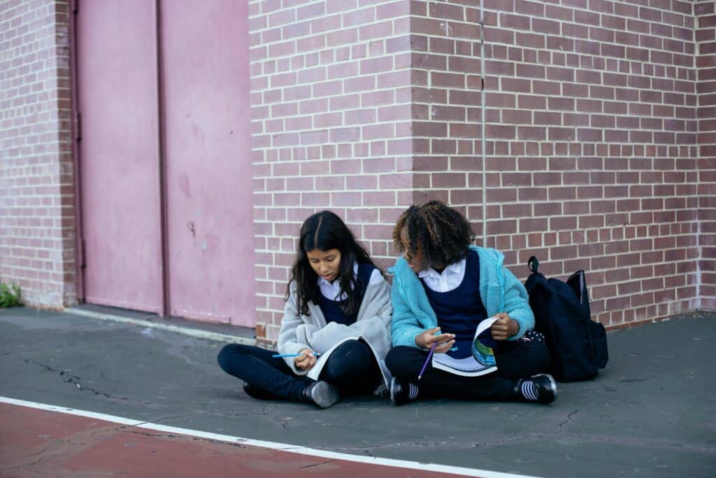 Two schoolgirls studying together outside in school uniforms.