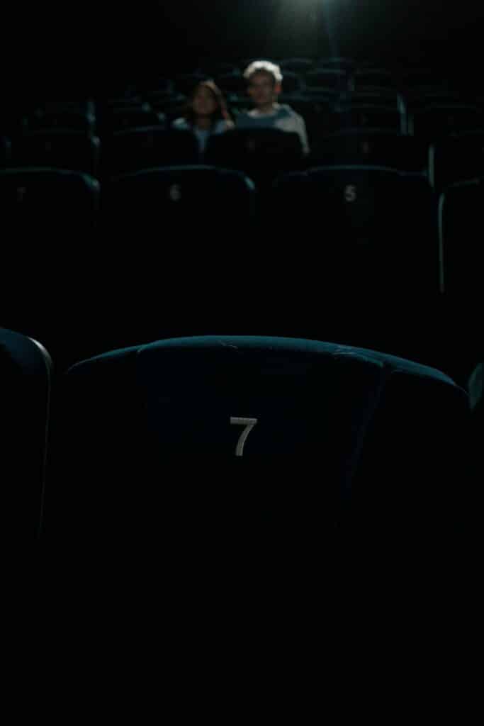 Low light image of a movie theater with empty seats and distant spectators, creating a dramatic ambiance.
