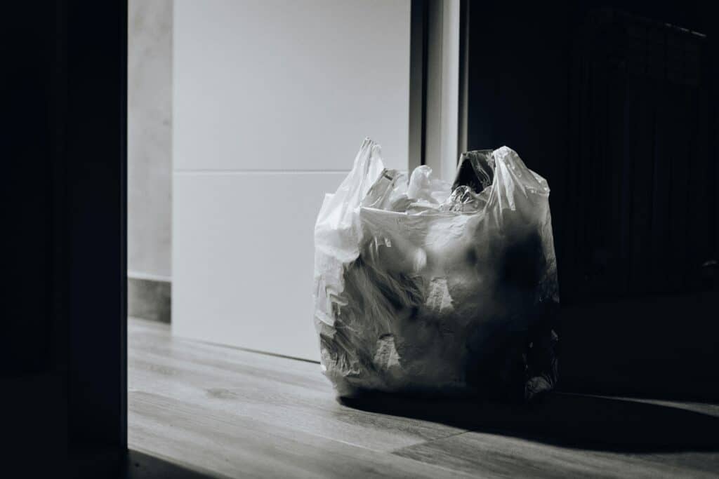 A dimly lit room containing a plastic bag filled with trash, emphasizing waste and recycling.