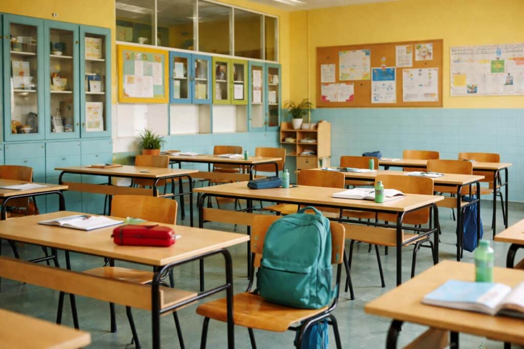 An empty classroom with wooden desks, chairs, and backpacks. Bright, welcoming atmosphere.
