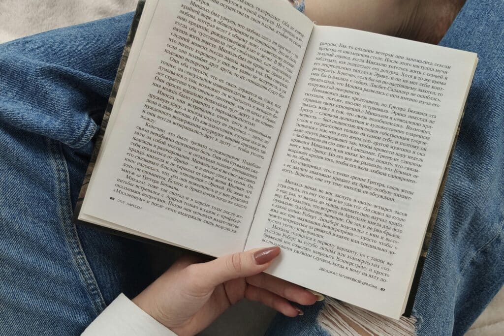 A woman enjoys a relaxing day reading a book while lounging indoors, dressed in casual jeans.