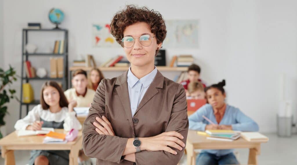 A confident teacher stands in front of students in a classroom setting.