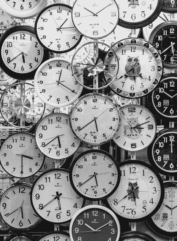 A black and white image displaying a diverse array of vintage wall clocks.