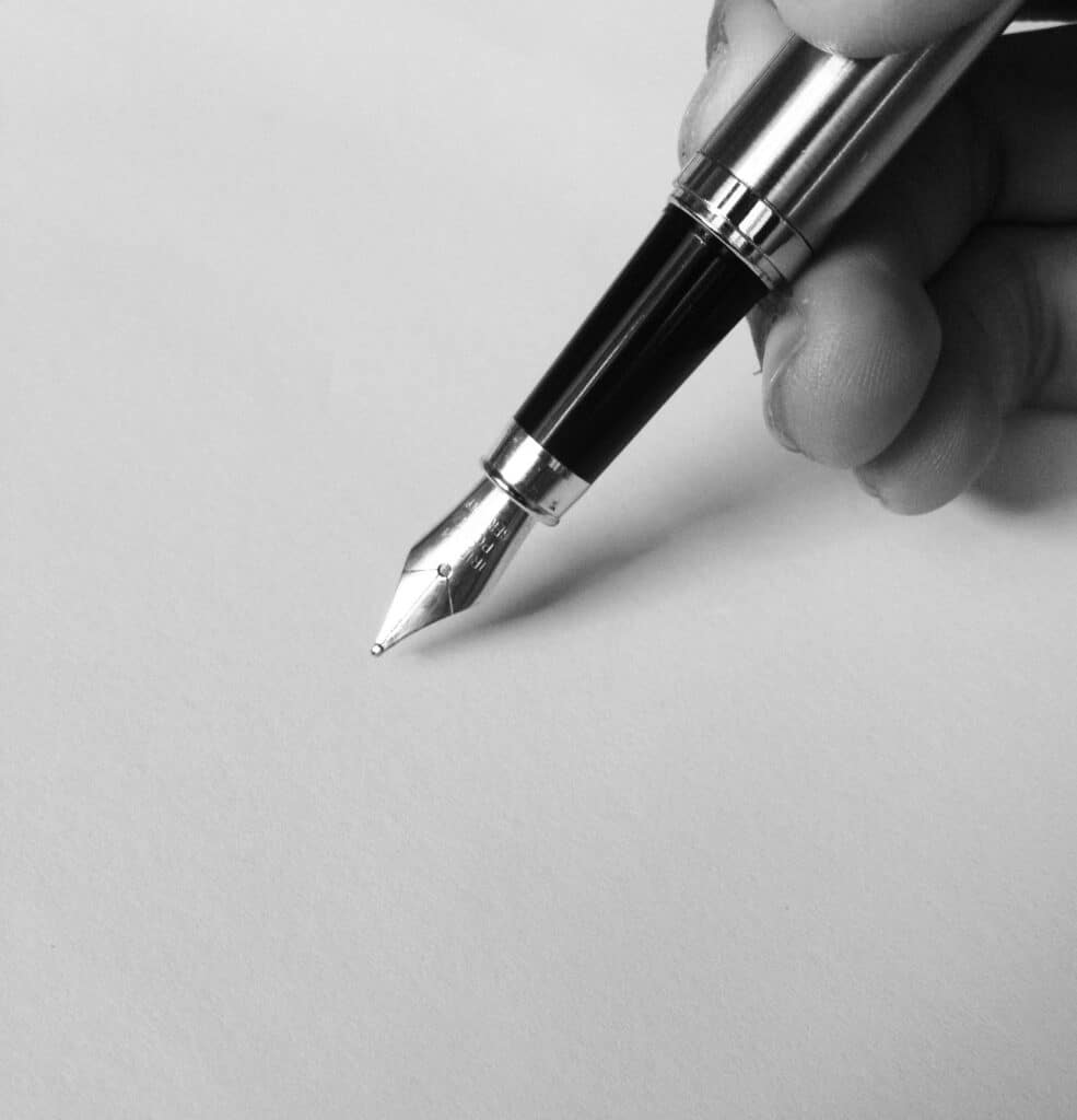 A close-up of a fountain pen writing on blank paper in black and white, capturing elegance.