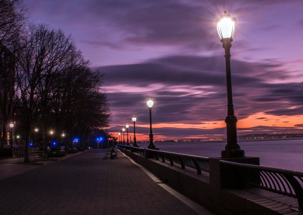 Dusk view of lamppost-lit path by the river at Robert Wagner Park, NYC.