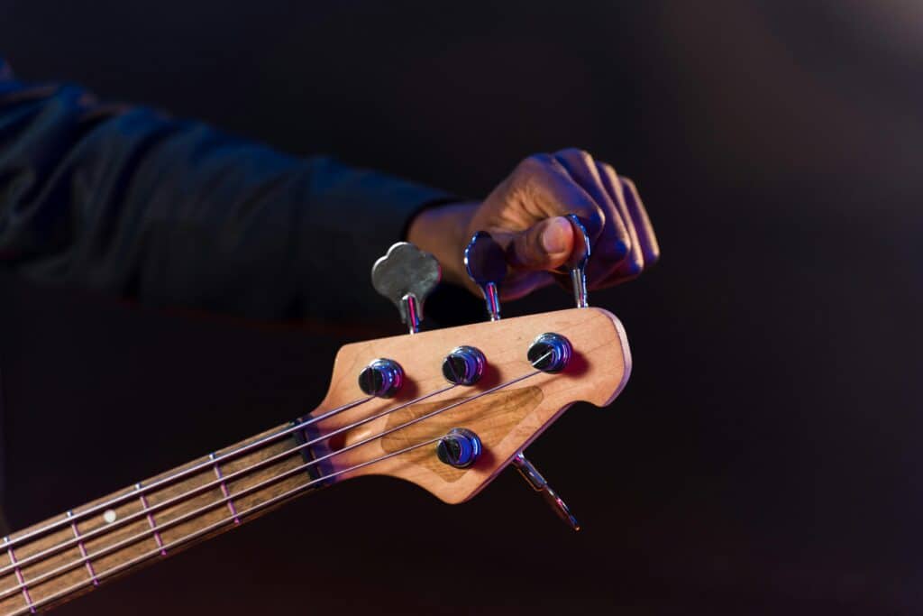 Detailed shot of a hand adjusting tuning pegs on a bass guitar's headstock with a dark background.