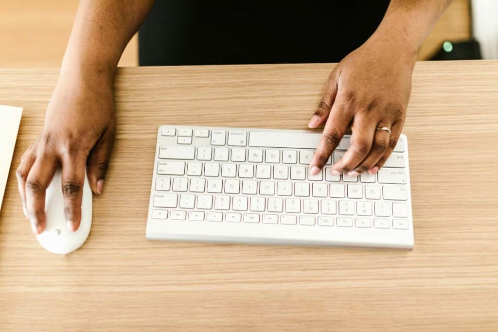 Hands typing on a white keyboard on wooden desk, ideal for business or tech themes.