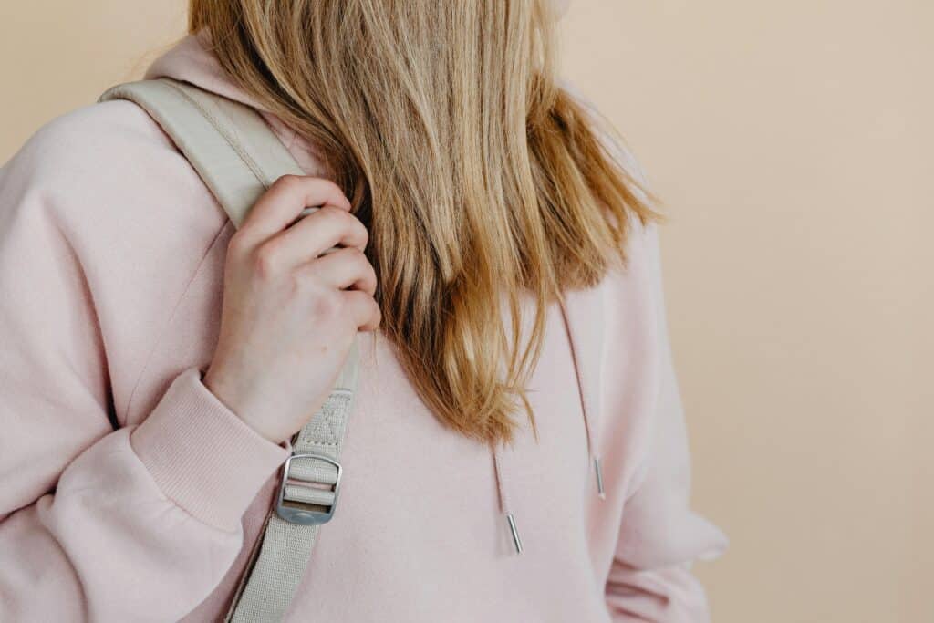 Close-up of a teenage girl holding a backpack strap in a pink hoodie. Studio setting.