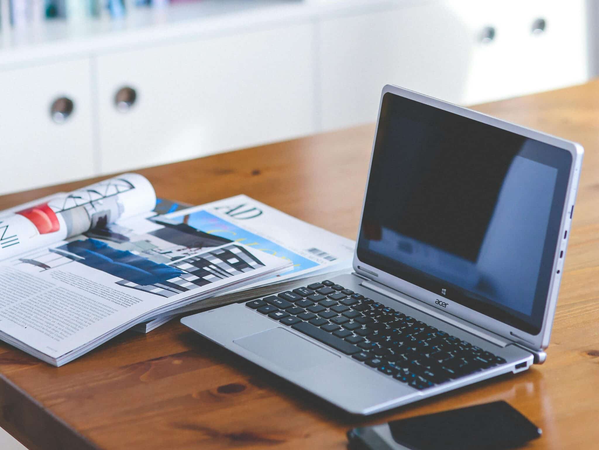 A stylish desk setup featuring a laptop, magazine, and bookshelf in a contemporary home office.