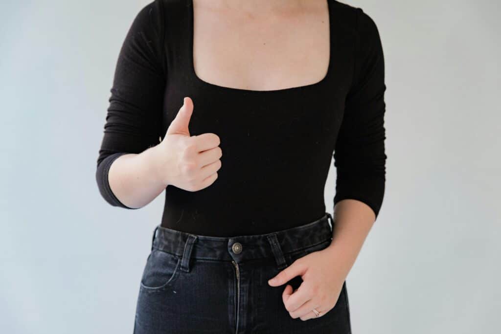 Close-up of a woman in a black outfit giving a thumbs up gesture indoors.