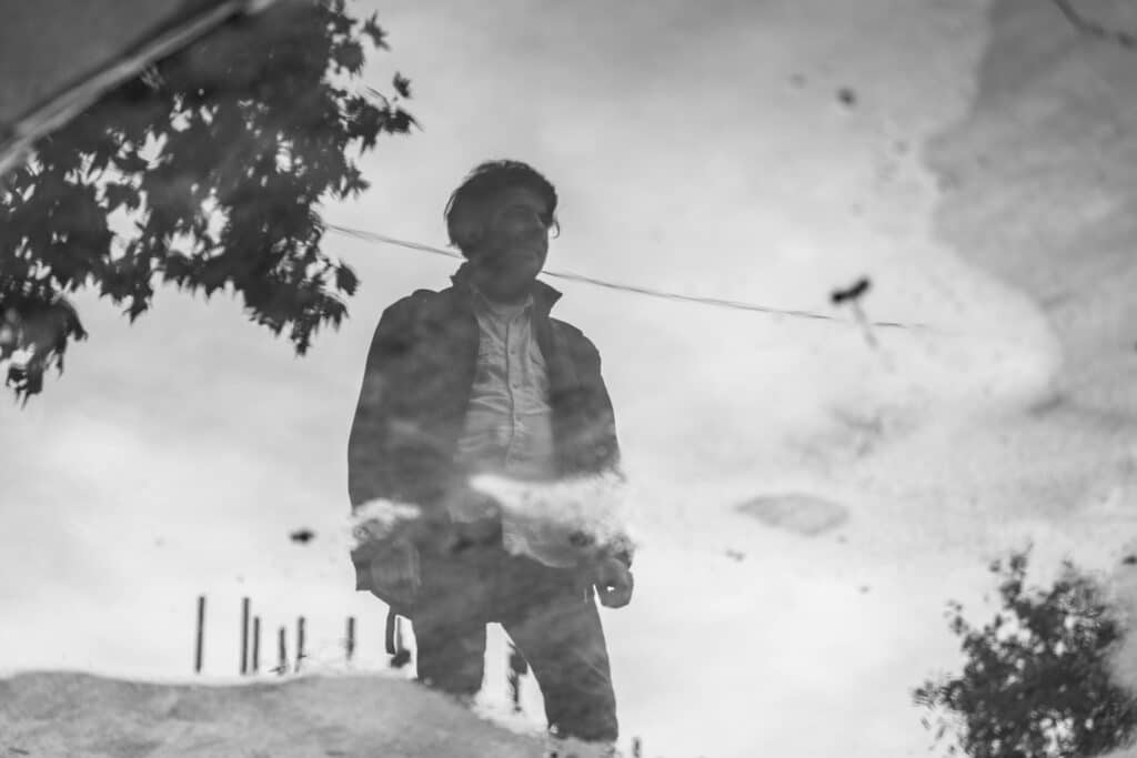 Black and white reflection of a man in a water puddle, creating a moody atmosphere.