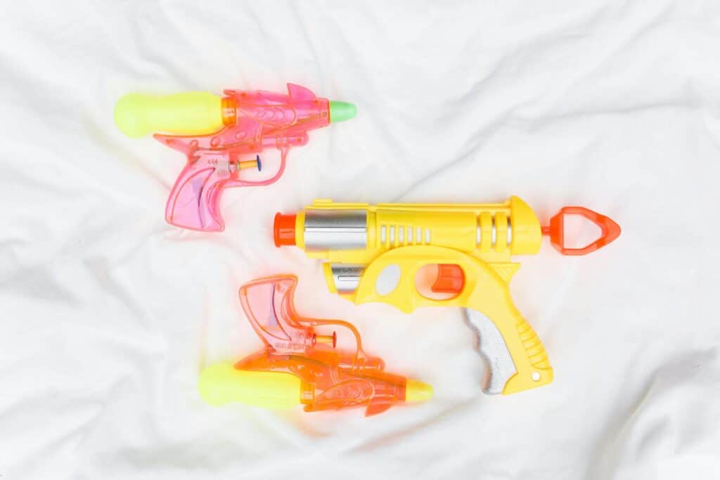 Bright plastic water guns arranged on a white fabric backdrop.
