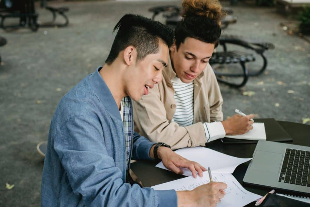 Two students working together on an assignment in a park, engaging in collaborative study.