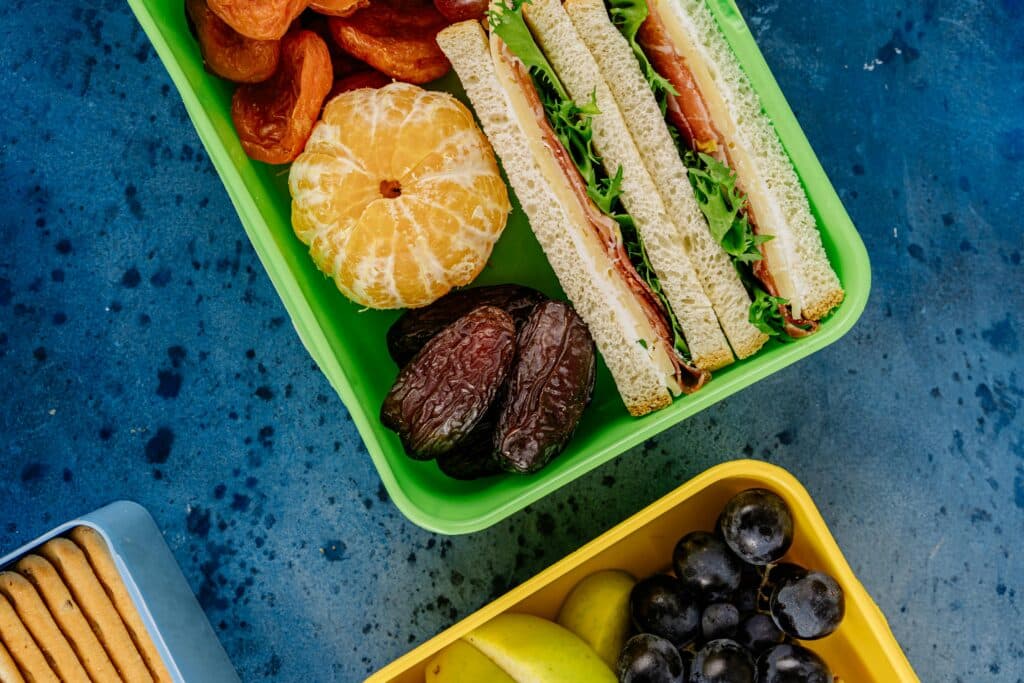 Top view of colorful lunch boxes filled with healthy sandwiches, fruits, and snacks.