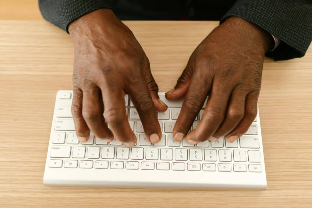 Close-up of hands typing on a wireless keyboard on a wooden desk.