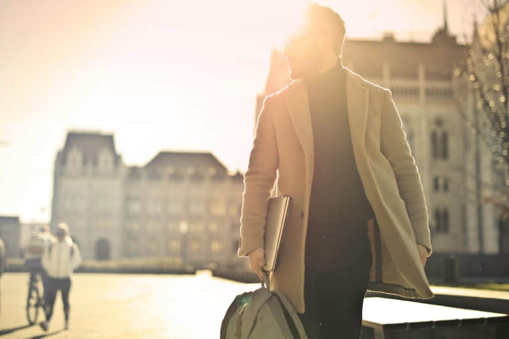 A businessman walks in front of a historic building in Budapest with sun glare illuminating the scene.