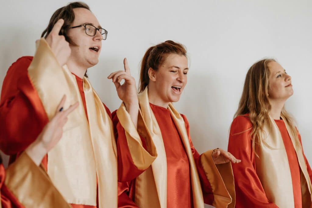 A choir group passionately singing together in red and gold robes indoors.
