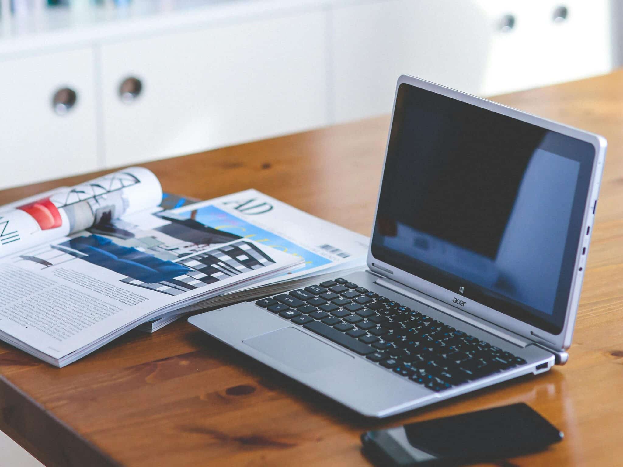 A stylish desk setup featuring a laptop, magazine, and bookshelf in a contemporary home office.
