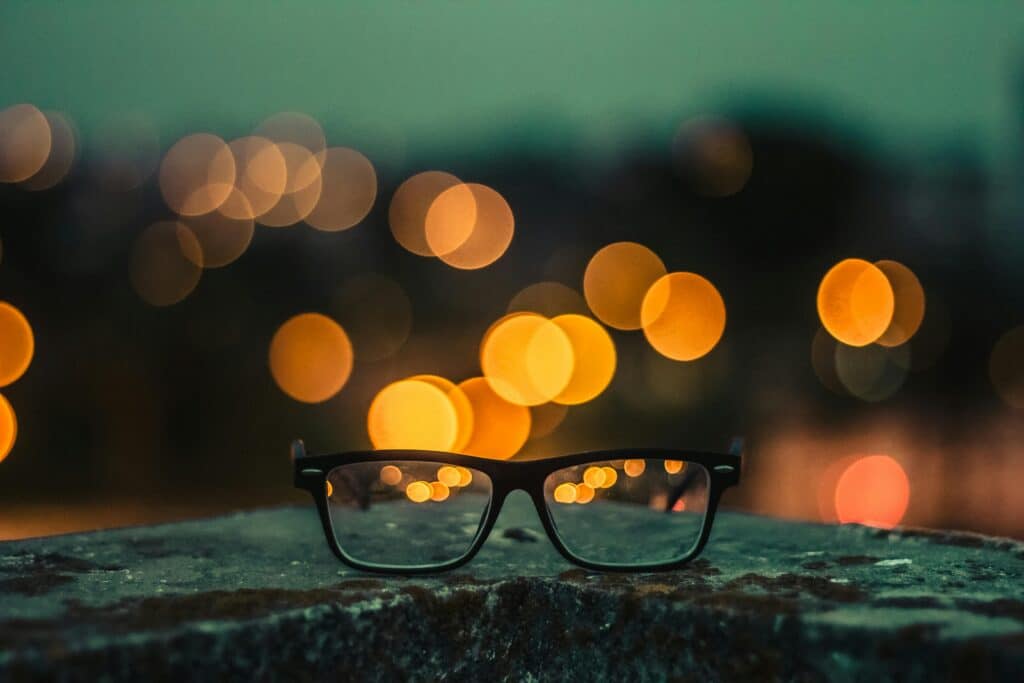 Eyeglasses placed on a stone surface, highlighted by a colorful bokeh light effect in the background.