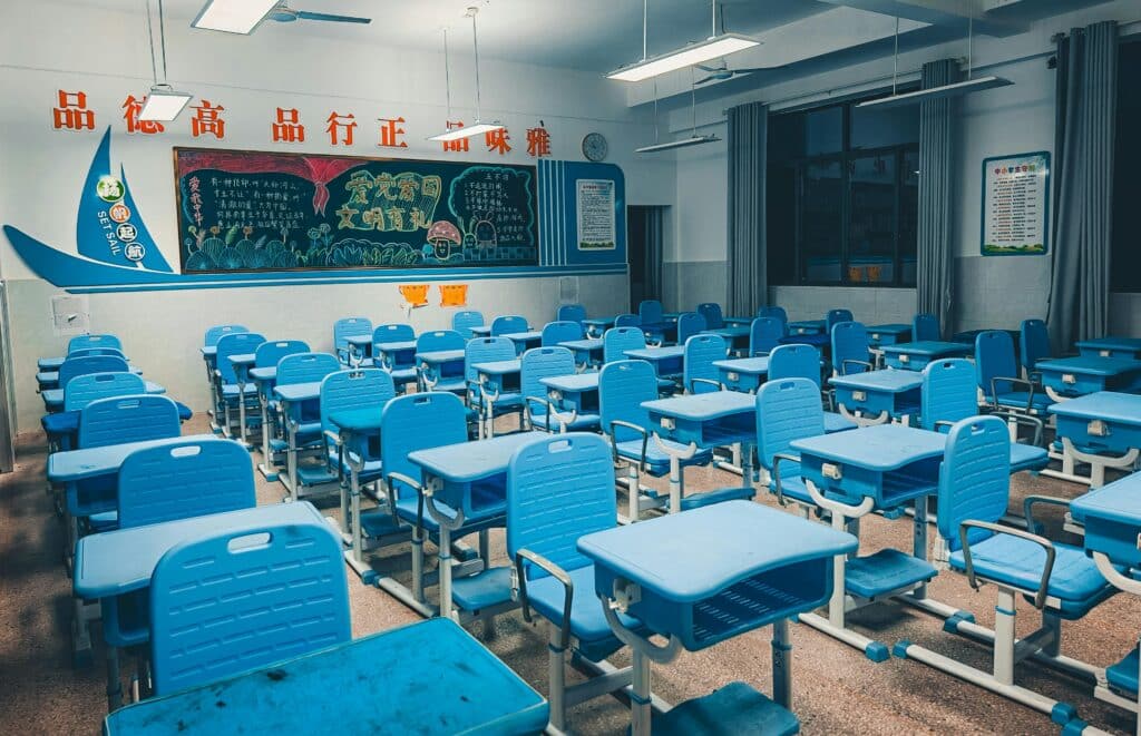 Spacious classroom with blue desks and vibrant decorated chalkboard, ready for students.