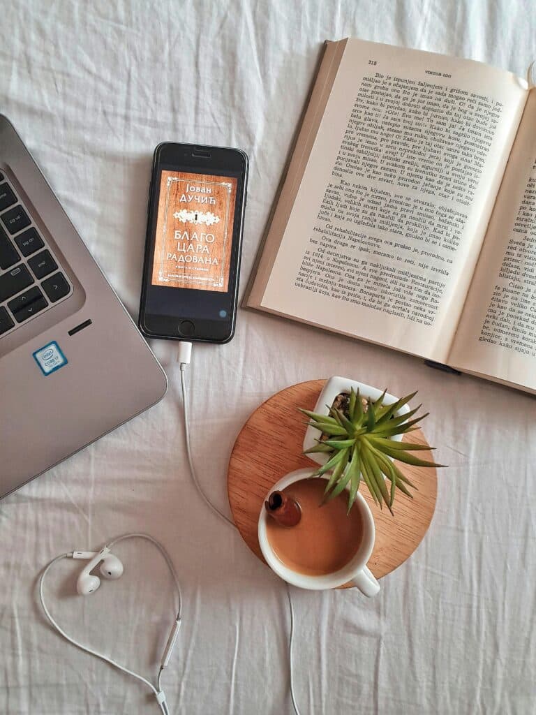 Relaxing workspace flat lay featuring a laptop, book, coffee cup, smartphone, and plant on a white surface.