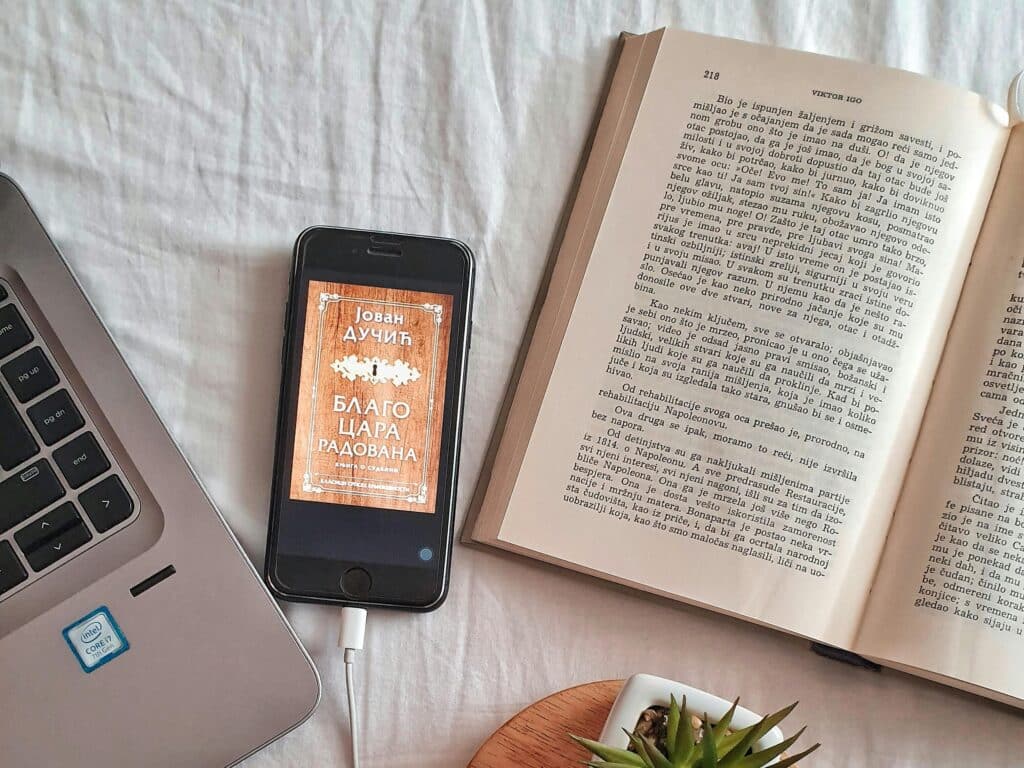 Relaxing workspace flat lay featuring a laptop, book, coffee cup, smartphone, and plant on a white surface.