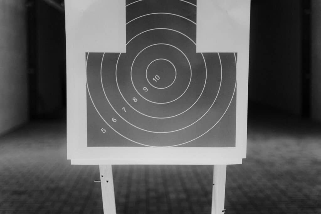 Black and white image of a shooting range target with numbered rings, highlighting aim precision.