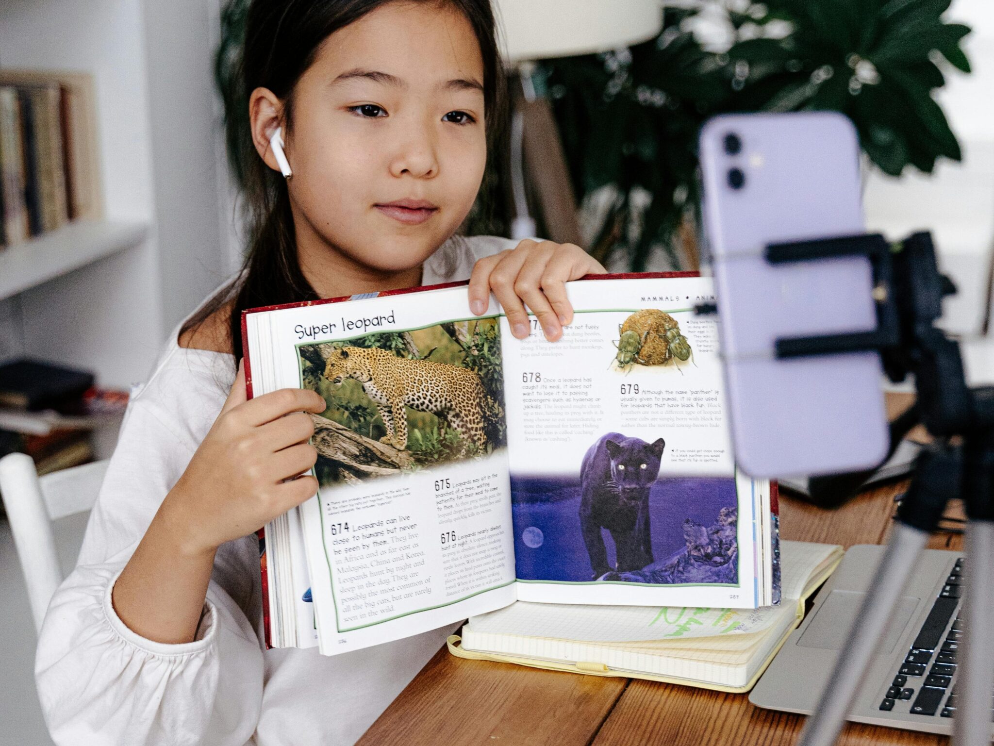 Young girl displays book during online class using smartphone and tripod.