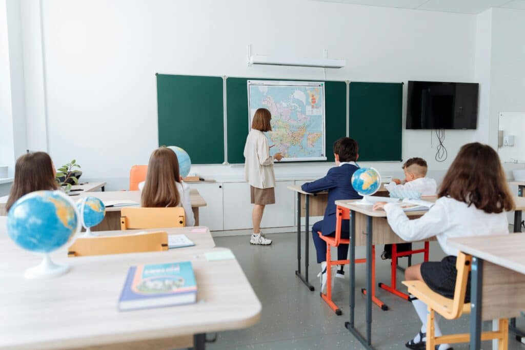 Students engaged in a geography lesson, focusing on a wall map in a classroom with globes and study materials.