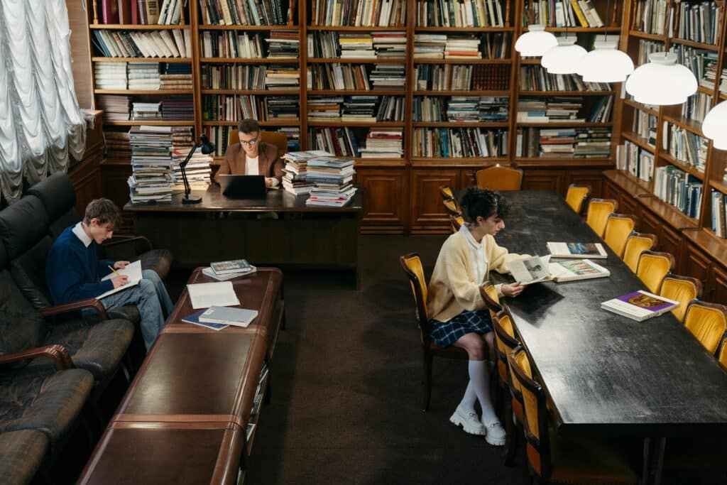 Three students engage in study at a cozy library with books lining the walls.