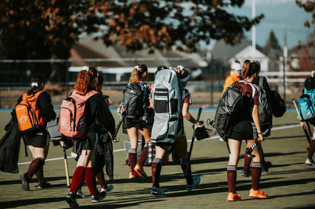 Group of young athletes with gear heading to field hockey practice.