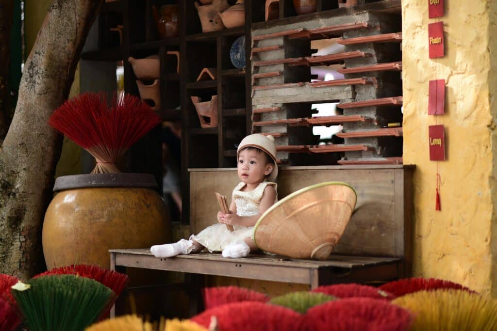 A young child sits among colorful incense sticks in a rustic setting, capturing cultural vibrancy.