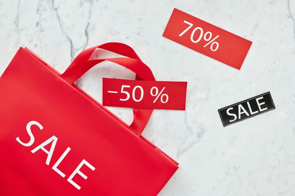 Red sale bag with 50% and 70% discount tags on marble background, perfect for retail promotions.